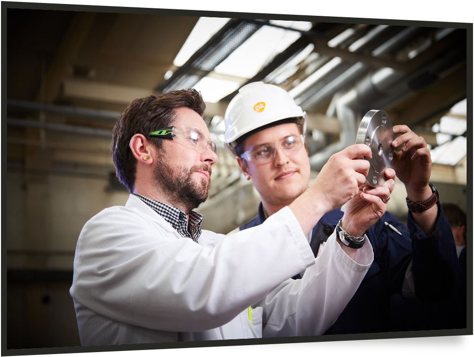2 male engineers in PPE looking at a piece of metal