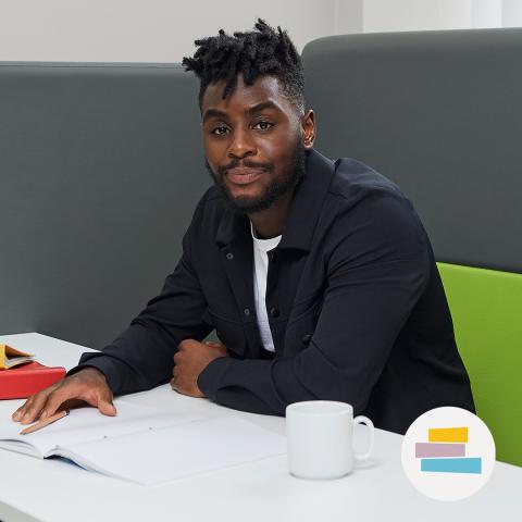 Young Black man in a black jacket sitting with his books and a coffee