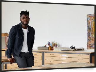 Young black man sitting on a table in an office, looking to camera